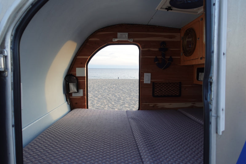 Cozy rv rental interior with bed and wood details, looking out to a serene sandy beach and calm ocean. — photo 10