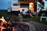 Friends relax by a warm campfire near their RV rental, showcasing illuminated van life on a peaceful evening.