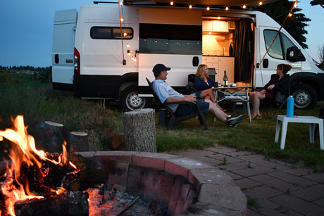 Friends relax by a warm campfire near their RV rental, showcasing illuminated van life on a peaceful evening.