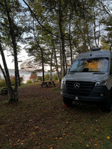 RV rental camper van parked by a misty lake, surrounded by autumn trees and a picnic table at a scenic campsite.