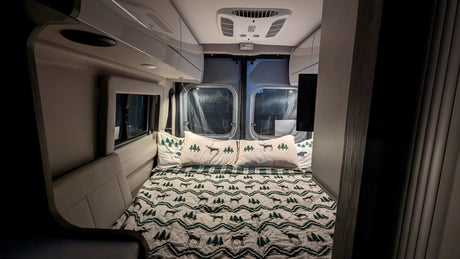 Cozy RV rental bedroom with deer & tree bedding, overhead AC, and rear windows, perfect for travel.
