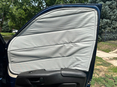 Inside an RV rental van's door, a light gray, quilted window cover provides essential privacy and insulation.