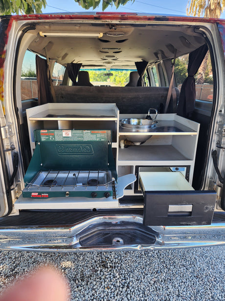This RV rental camper van features a clever kitchen setup with a Coleman propane stove, sink, and Dometic cooler.