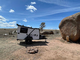 White Tiger Moth rv rental camper trailer parked in a rocky outdoor landscape under a blue sky.