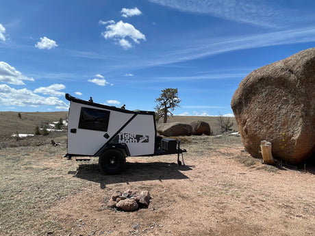 White Tiger Moth rv rental camper trailer parked in a rocky outdoor landscape under a blue sky.