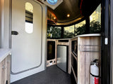 Modern rv rental interior: kitchen with fridge, counter space, large windows, and safety fire extinguisher.