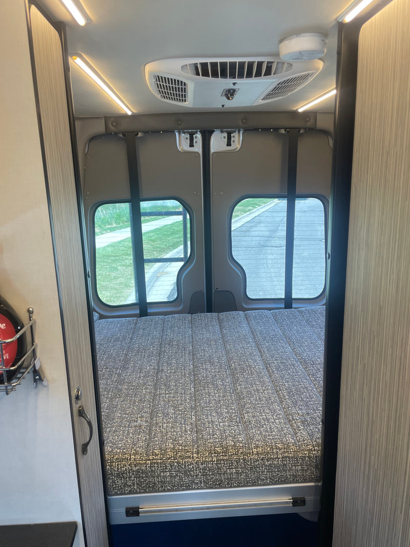Interior of an RV rental camper van showing the rear bed area. Features include a textured mattress, ceiling AC, and lighting. — photo 9