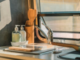 RV rental kitchen: A clean sink area with soap bottles, wooden utensils, and a sunny window with a screen.