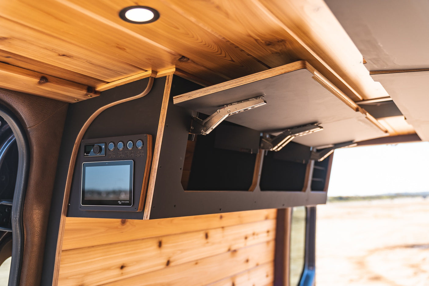 Inside a modern RV rental: wood-paneled ceiling, lift-up overhead storage, and integrated digital control panel.