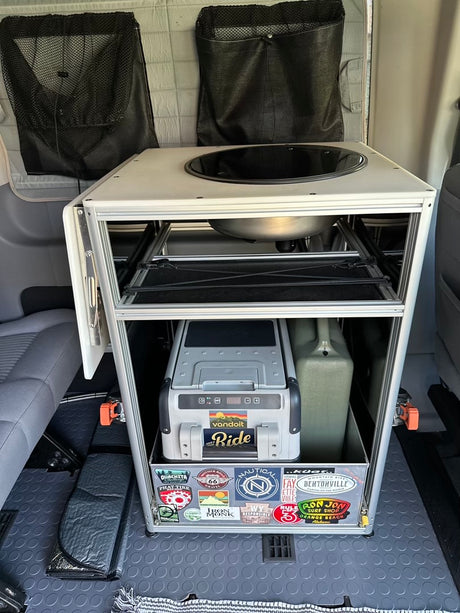 Compact RV rental kitchen module with a sink, pull-out fridge, and water tank for efficient campervan adventures.