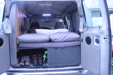 View into a functional RV rental's camper van interior, showcasing a bed, pillows, and organized storage for mobile living.