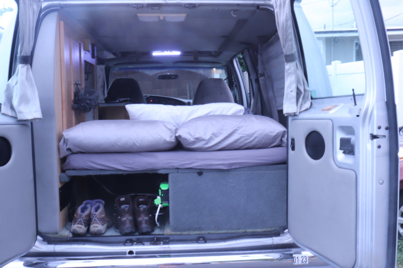 View into a functional RV rental's camper van interior, showcasing a bed, pillows, and organized storage for mobile living. — photo 17