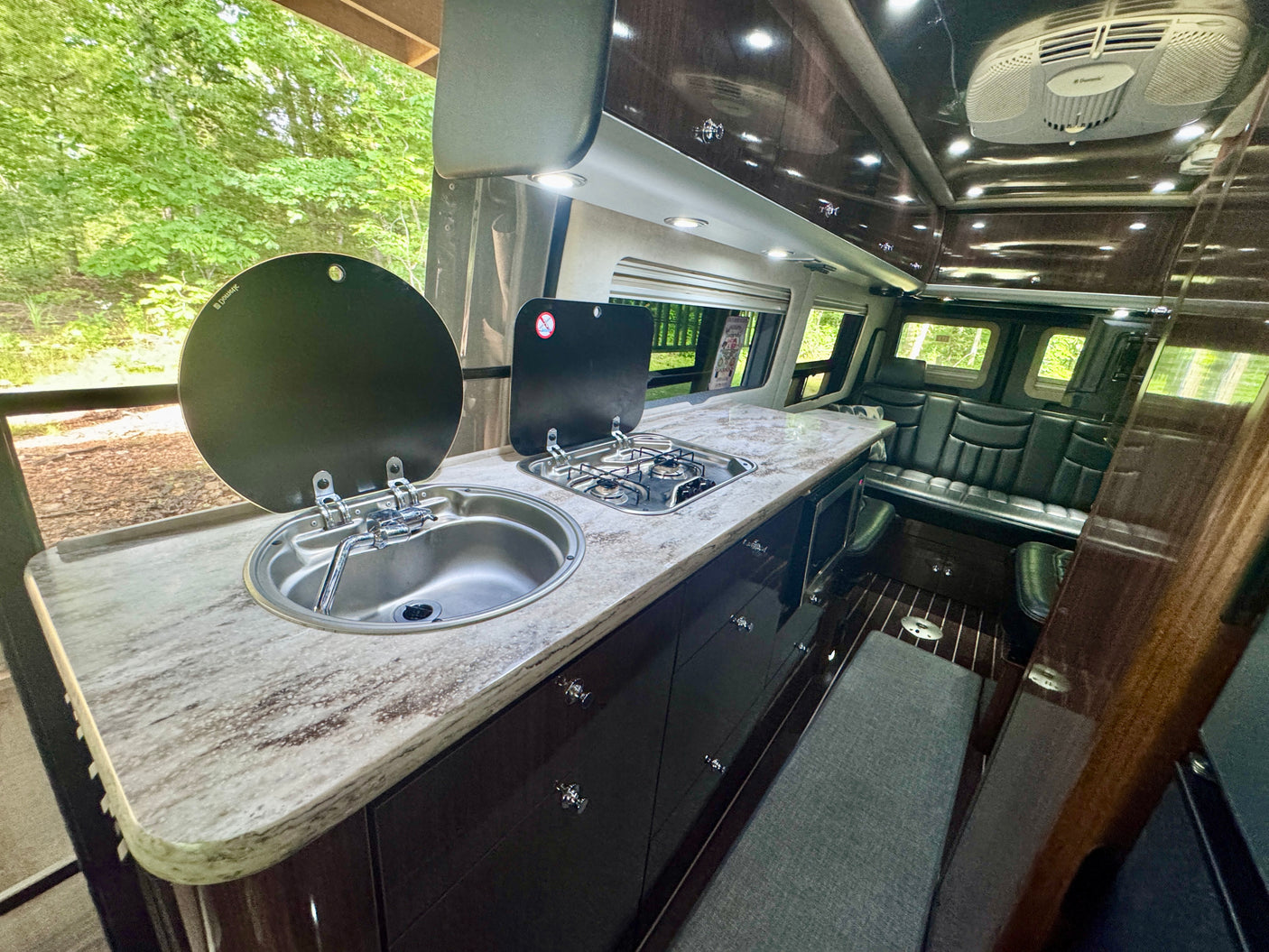 Modern rv rental interior with a compact kitchen featuring a sink and stove, plus comfortable seating and dark wood accents.