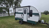 Compact Sun Lite travel trailer, ideal for an RV rental adventure, parked on grass with trees & fence background. Ready for camping!