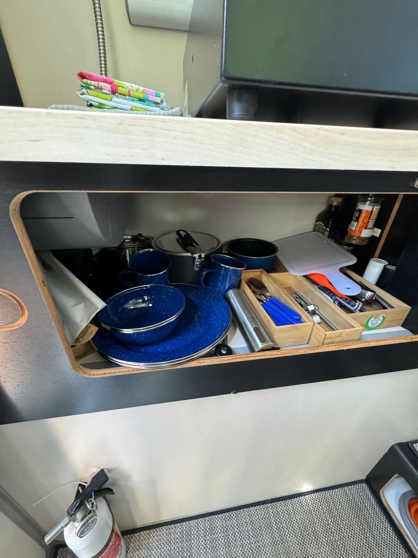An RV rental's kitchen cabinet is open, showing neatly organized camping gear including blue enamelware, utensils, and cookware. — photo 11