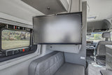 Inside a modern RV rental: TV, gray bench seat, and a window framing a rocky landscape. Comfort for your mobile adventures.