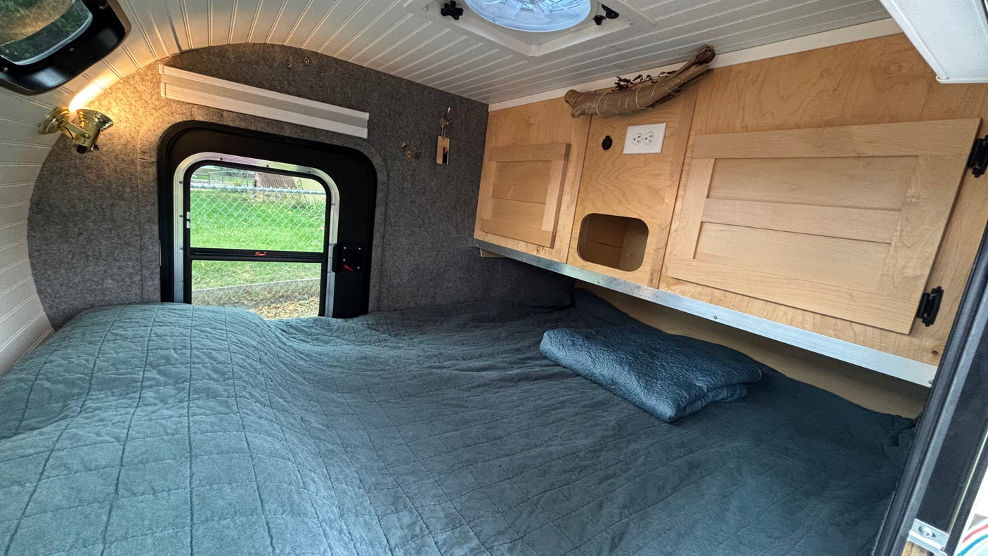 Cozy RV rental interior: a comfy bed, wooden cabinets, and a window view, perfect for compact travel adventures.