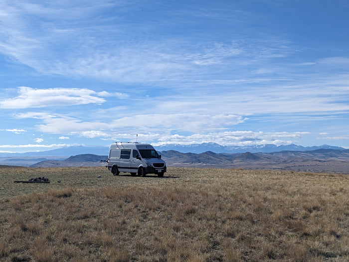 Freedom on wheels! An RV rental Sprinter van in a golden field, with snow-capped mountains under a blue sky.