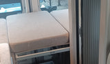Comfortable light beige bed/seating in an RV rental, featuring a THOR frame, outdoor window view, and a rolling side door.