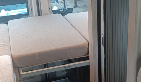 Comfortable light beige bed/seating in an RV rental, featuring a THOR frame, outdoor window view, and a rolling side door.