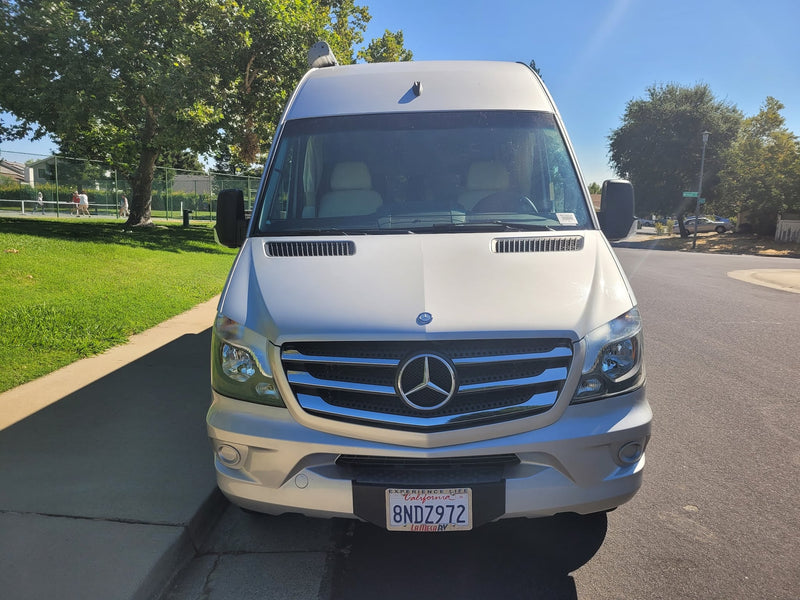  parked on a sunny day with a park and residential street in background.|Silver Mercedes Sprinter RV rental on a sunny suburban street.|A silver Mercedes-Benz Sprinter camper van — photo 2