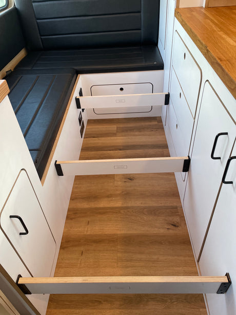 RV rental: Camper interior with black bench, wood floor, and modular bed slat supports for a versatile living space.