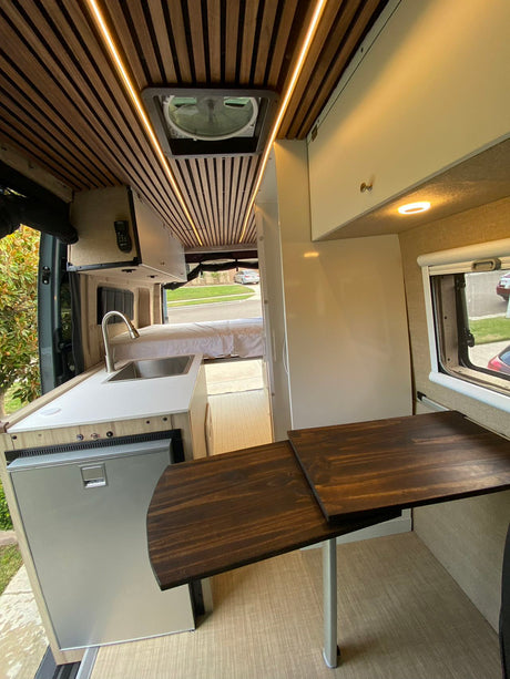 Explore this stylish RV rental interior, showcasing a modern kitchen, comfortable bed, and versatile dining space.