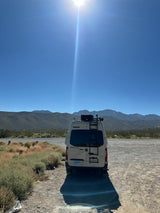 A Winnebago Revel RV rental van in a sunny desert landscape with distant mountains under a clear blue sky.