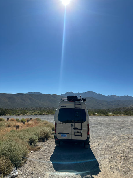 A Winnebago Revel RV rental van in a sunny desert landscape with distant mountains under a clear blue sky.