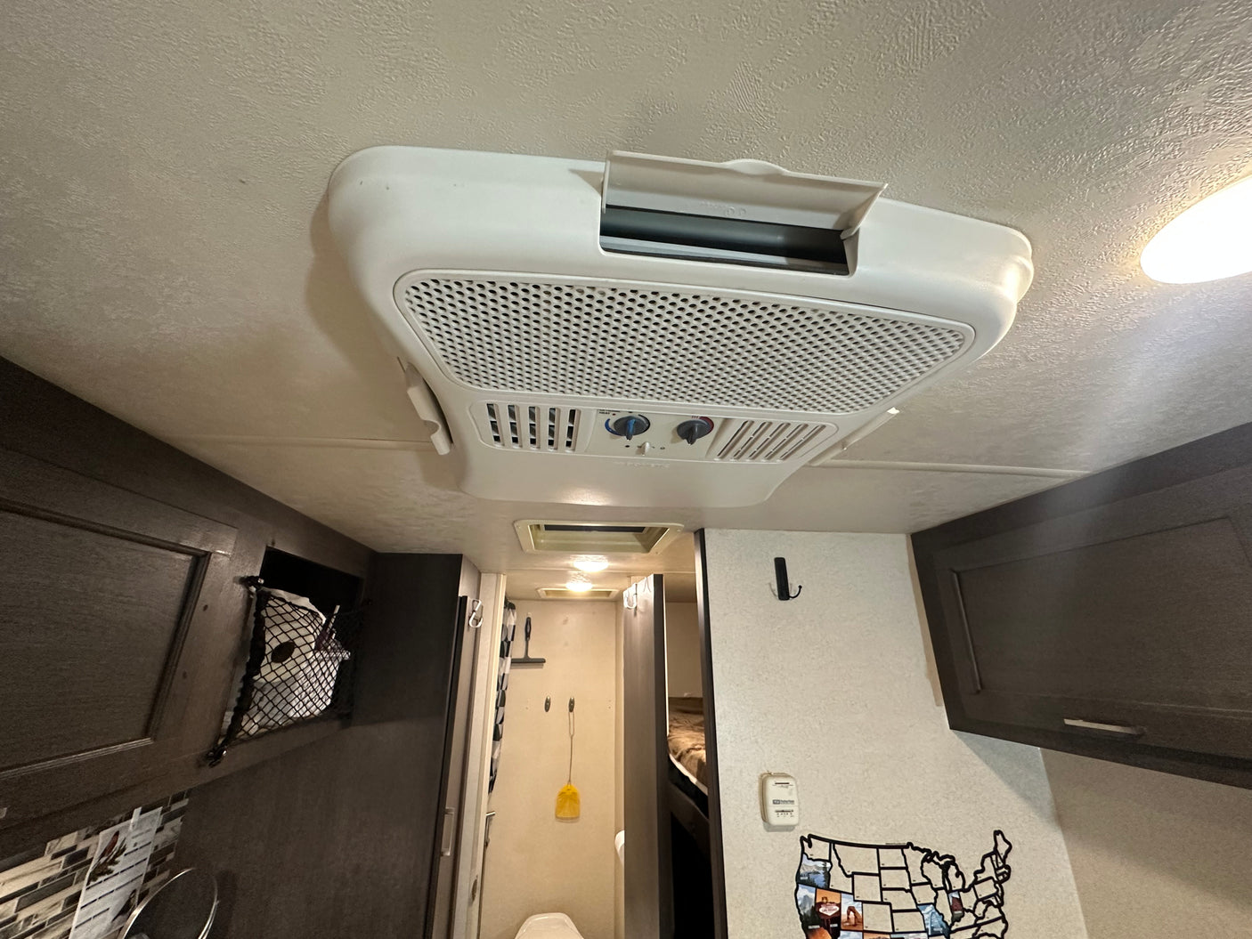 Interior of an RV rental: a bright white ceiling with an AC unit, modern dark cabinets, and travel-themed wall decor for comfy stays.