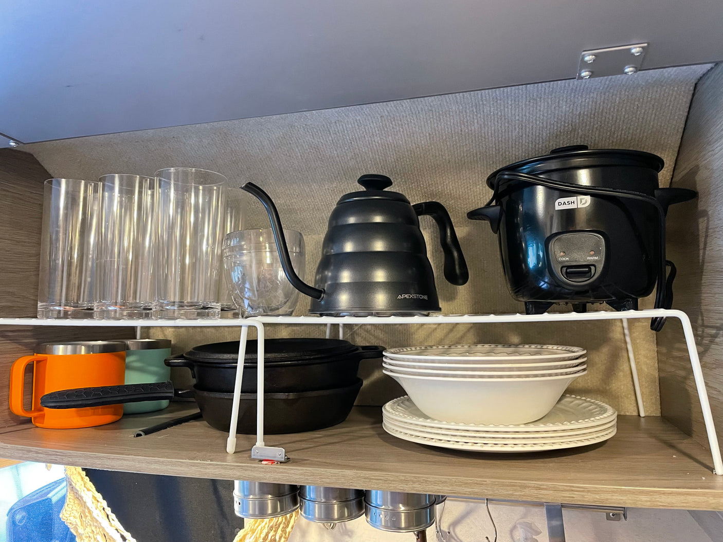 RV rental kitchen: organized shelves with clear glasses, Apexstone kettle, Dash rice cooker, mugs, cast iron, and dishes.