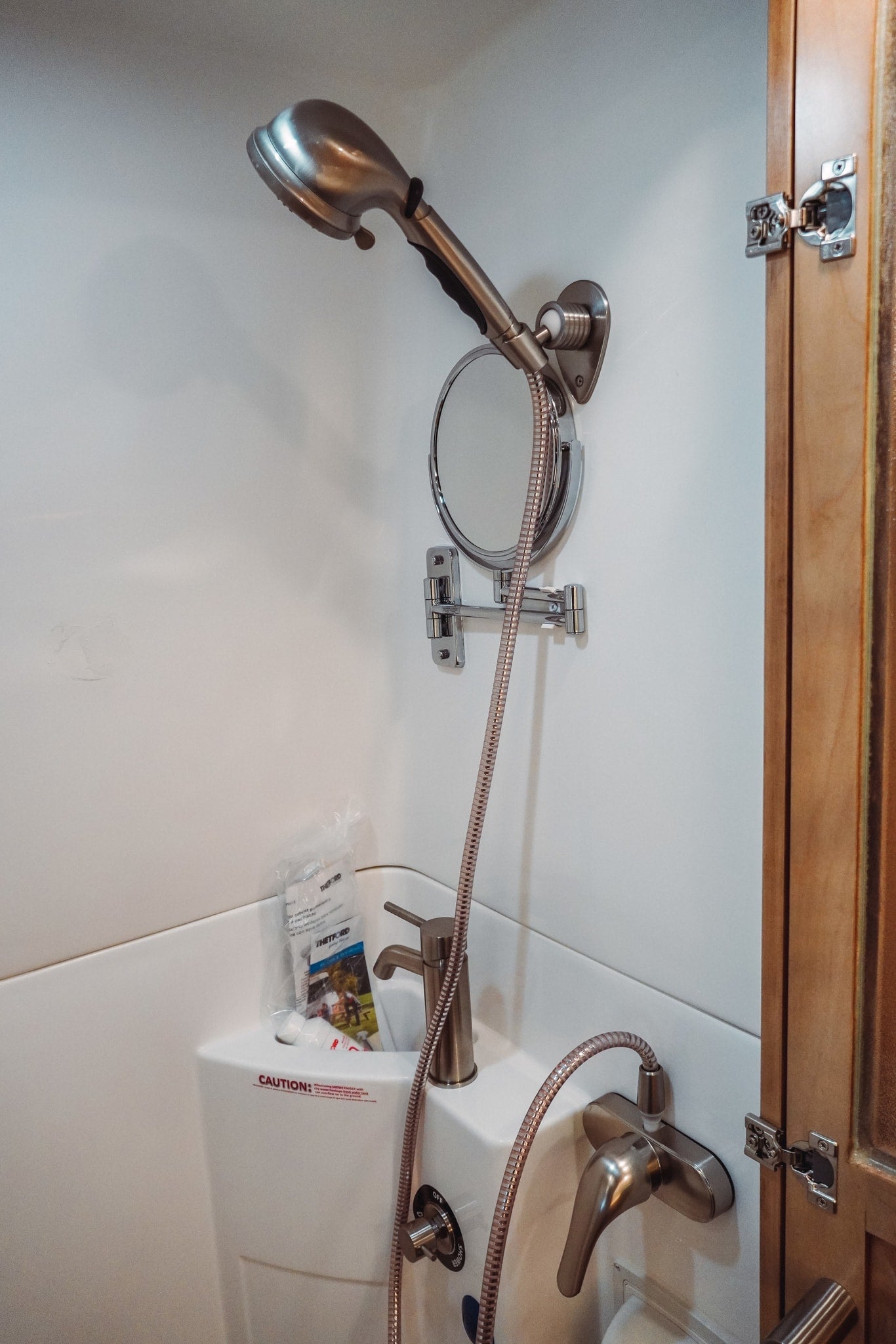 Inside a compact RV rental bathroom, showing a shower, sink, adjustable mirror, and various controls. — photo 6