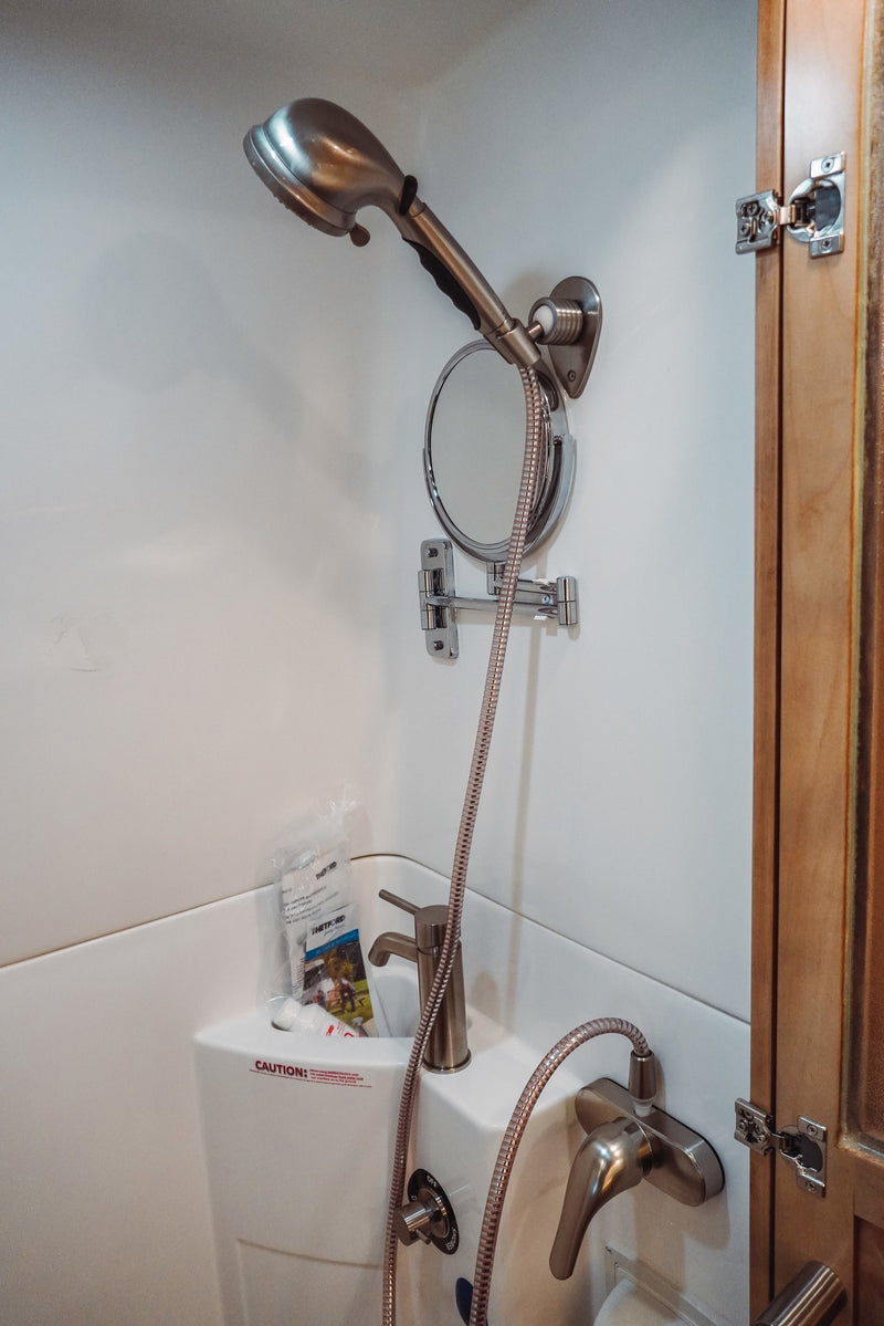 Inside a compact RV rental bathroom, showing a shower, sink, adjustable mirror, and various controls. — photo 6