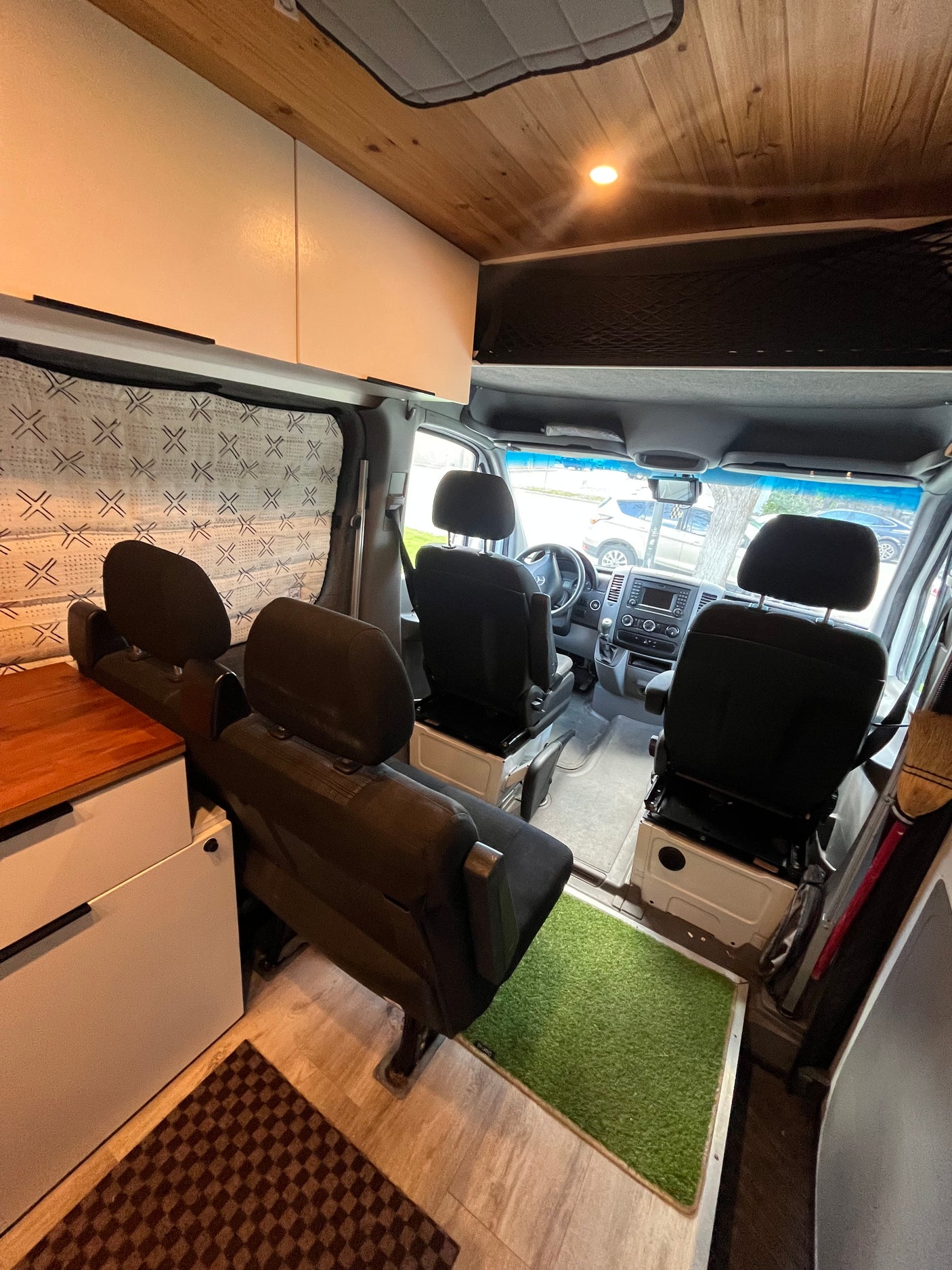 RV rental: custom camper van interior with driver's cab, four black passenger seats, wood ceiling & white cabinetry.
