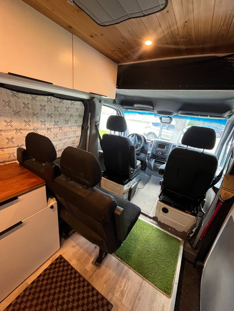 RV rental: custom camper van interior with driver's cab, four black passenger seats, wood ceiling & white cabinetry.