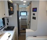 Inside an RV rental: a bright, modern interior with a full kitchen, control panels, and a cozy rear bed/seating area.
