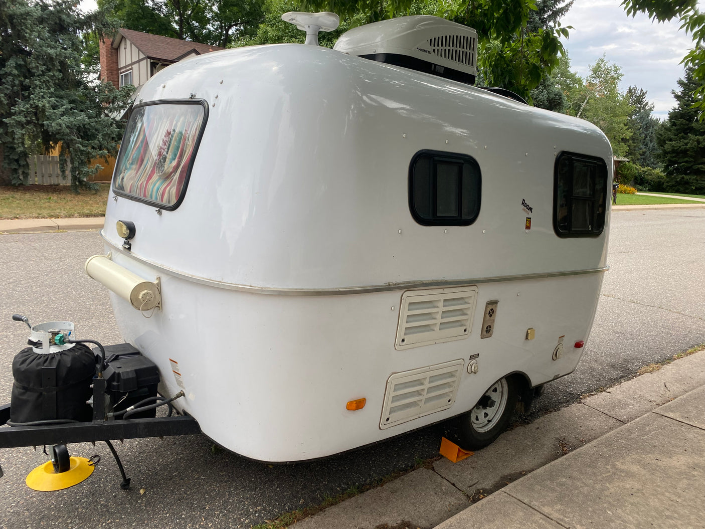 A sleek white travel trailer, ready for an RV rental getaway, parked curbside with a house & trees in the background.
