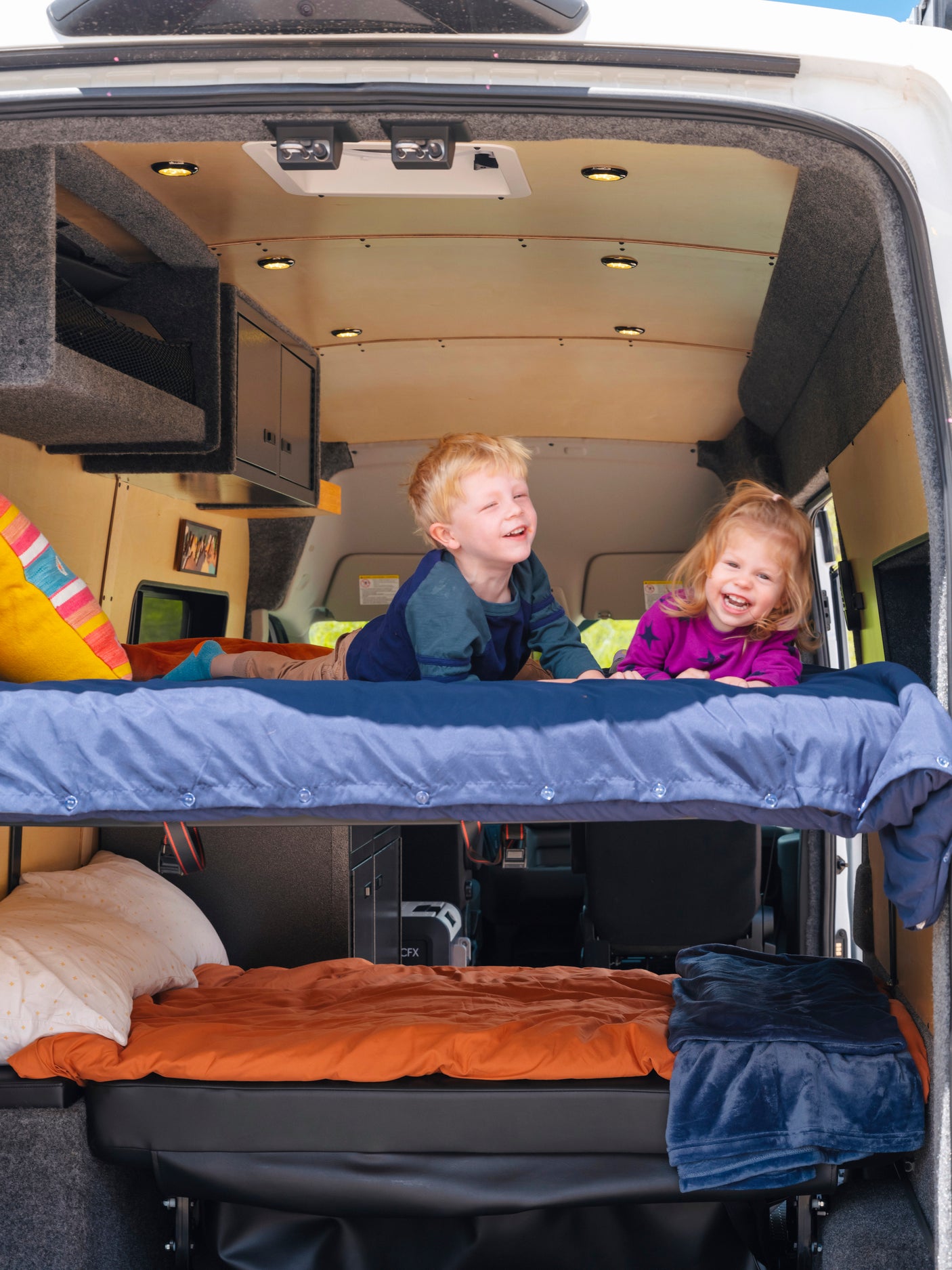 Two smiling children on bunk beds in an RV rental, showcasing a family-friendly interior for road trips.