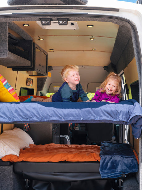 Two smiling children on bunk beds in an RV rental, showcasing a family-friendly interior for road trips.