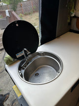 RV rental: Compact sink with faucet, lifted cover, & countertop. Practical for mobile kitchen needs in a camper.