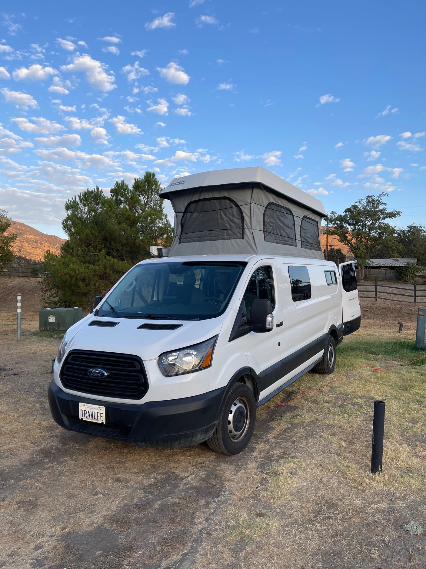 White Ford Transit pop-top camper van, ideal for RV rental adventures, parked in a scenic outdoor setting.