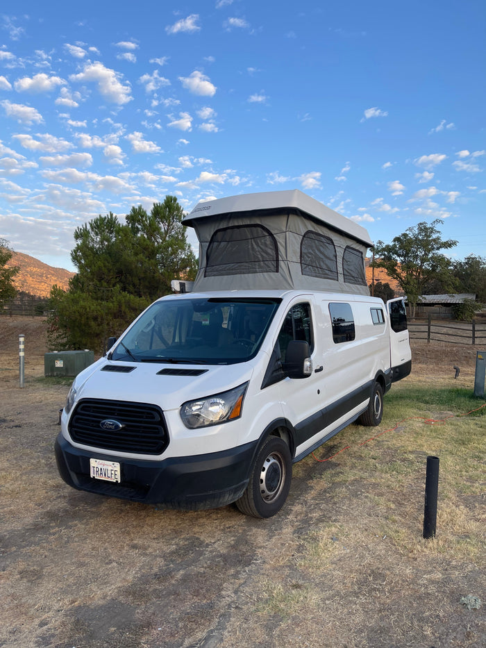 White Ford Transit pop-top camper van, ideal for RV rental adventures, parked in a scenic outdoor setting.