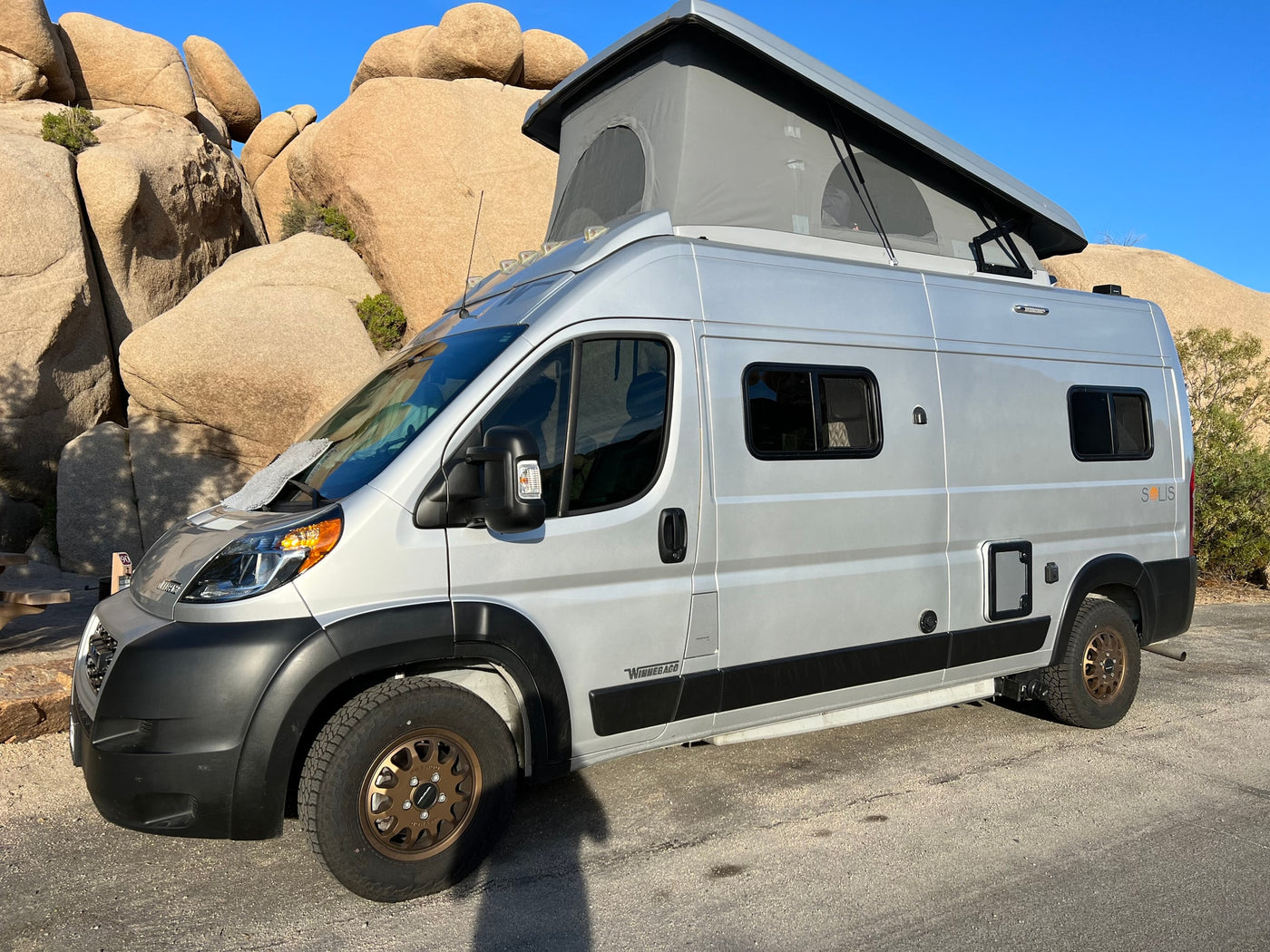 Silver Winnebago Solis RV rental with pop-top tent parked amidst large desert rock formations. — photo 8
