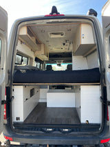 Modern camper van interior, showcasing a raised bed, storage units, and ceiling amenities. Perfect for an RV rental adventure.