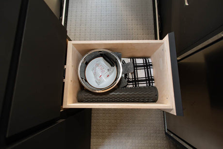 Organized wooden drawer in an RV rental, showing kitchen essentials: pot, measuring cup, towel, and silicone mat.