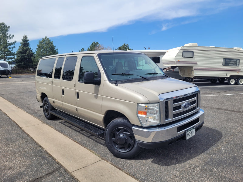 A tan Ford van is parked in a sunny RV rental lot, with large recreational vehicles in the background. — photo 6