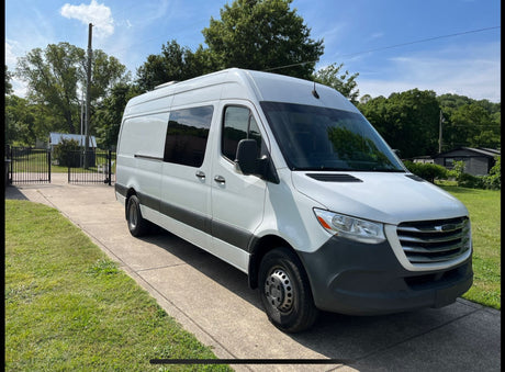 White Mercedes-Benz Sprinter camper van for RV rental, parked on a sunny driveway with trees and sky.