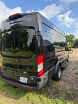 Black Ford Transit van for RV rental, detailed from the rear, reflecting sky & trees on its sleek surface.