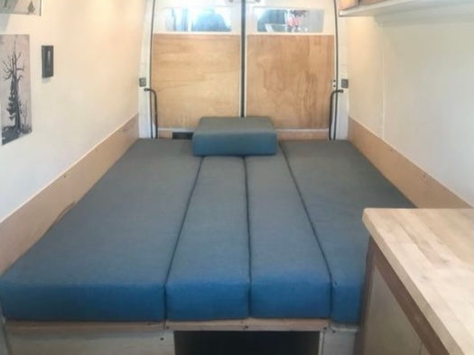 Inside an RV rental, featuring a versatile blue cushion bed/lounge, wood paneling, and visible rear doors.
