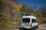 White RV rental van parked on a dirt road by a Sierra National Forest sign, surrounded by hillsides vibrant with orange wildflowers.